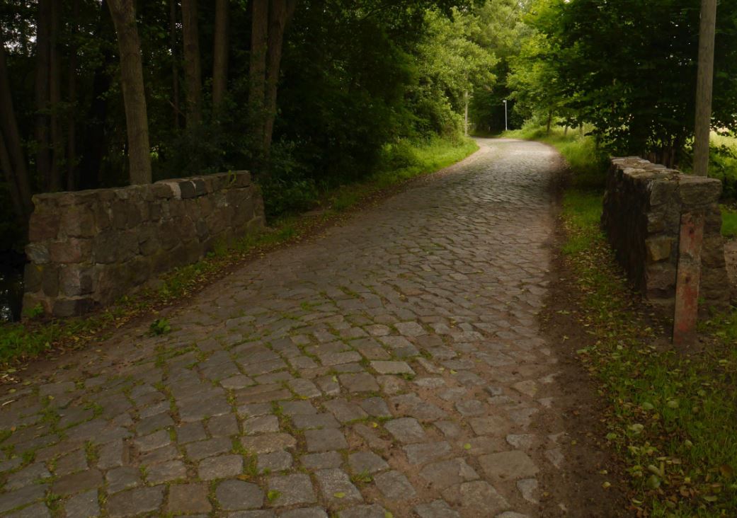 Eine alte Straße: Die Straße besteht aus großen Steinen. Zwischen den Steinen wächst grünes Gras.