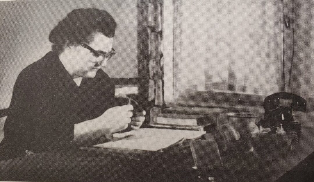 Ein Foto der Archäologin Dr. Sieglind Kramer, die an ihrem Schreibtisch sitzt und einen Gegenstand genau betrachtet.